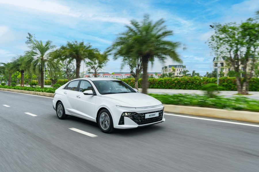 New Hyundai Accent màu trắng chạy trên đường có hàng cây xanh